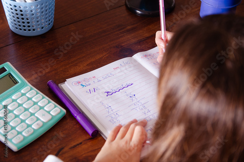 A young girl doing her maths homework using a calculator. 