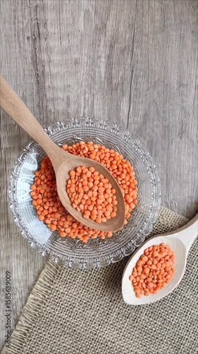 Dried red lentils in a decorative glass plate and wooden spoons on a gray background