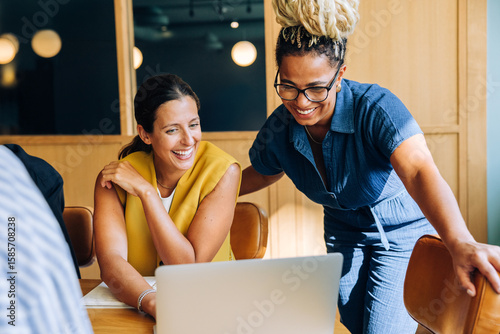 Fotografie Two professional women smiling and working together at a desk with a laptop