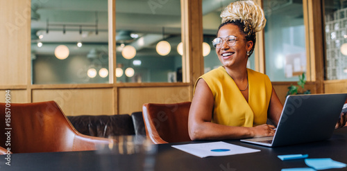 Confident professional woman smiling and working on a laptop in the office