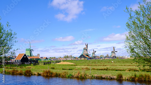 View of old Dutch windmills and water canals against blue sky in Holland. Zaanse Schans, Zaanstad, province North Holland, Netherlands.