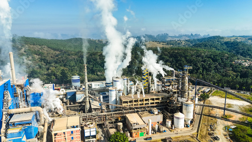 Visão aérea de uma fábrica de papel e celulose com grande estrutura e chaminés, representando a importância da produção industrial no cenário econômico.