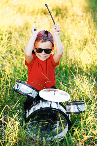 Beautiful smiling happy young little boy playing on the drums. Expressive Drummer Guy Playing Drums at Sunset. Rock Band Music Artist Learning a New Drum Solo