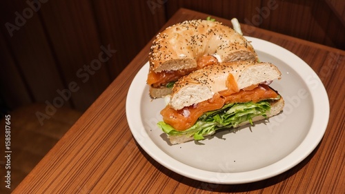 close up of a sesame and pumpkin seed bagel with lecttuce, smoked salmon and avocado on a plate cut in two two half showing the surface area with copy space