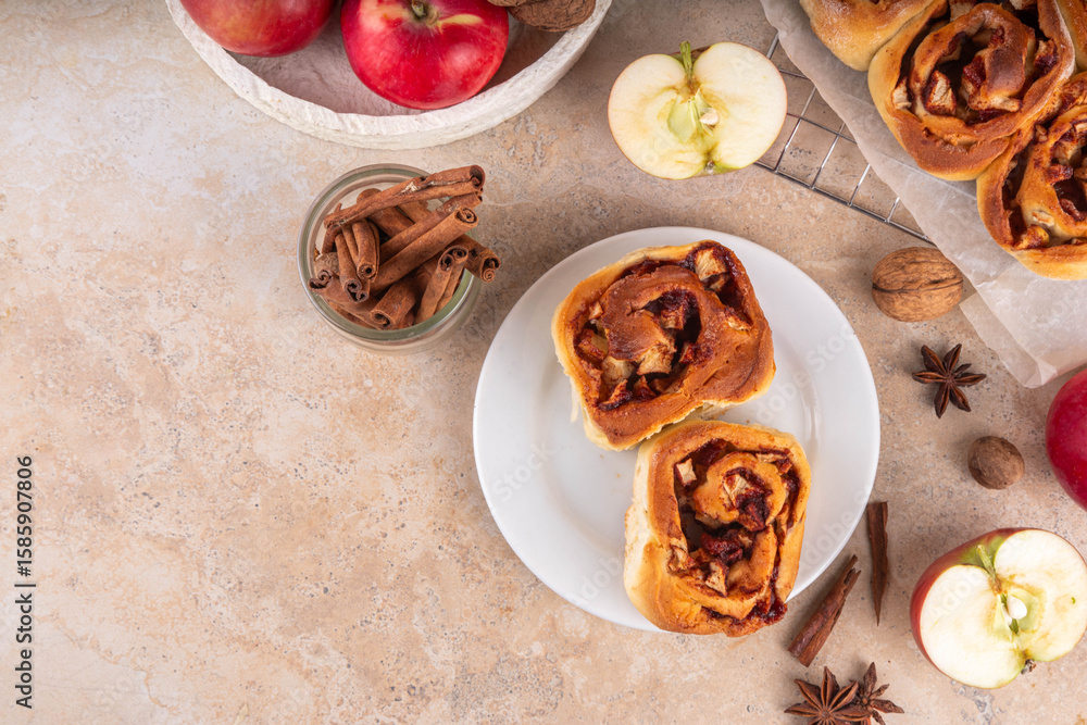 Fototapeta premium Apple cinnamon roll, sweet cinnabon buns with apple filling. Viral apple pie rolled buns, on beige table with cinnamon sticks, apples, nuts and spices