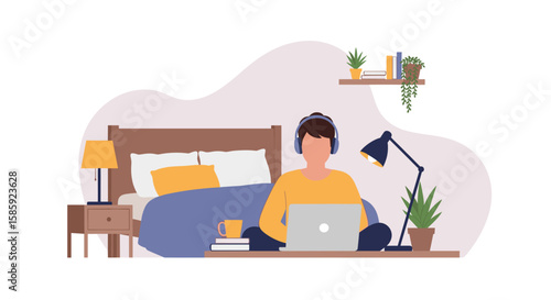 A young man with headphones sits in front of his bed, working on a laptop in a relaxed home environment, indicating remote work or online learning.