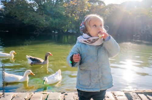 A little girl is standing by a pond with ducks