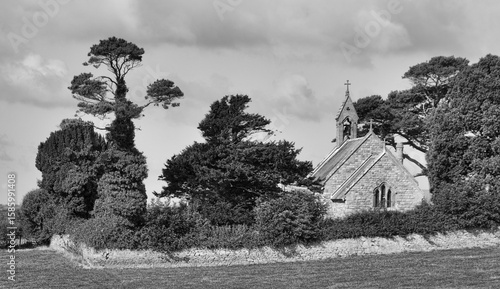 A grayscale image of a church surrounded by trees and a stone wall.