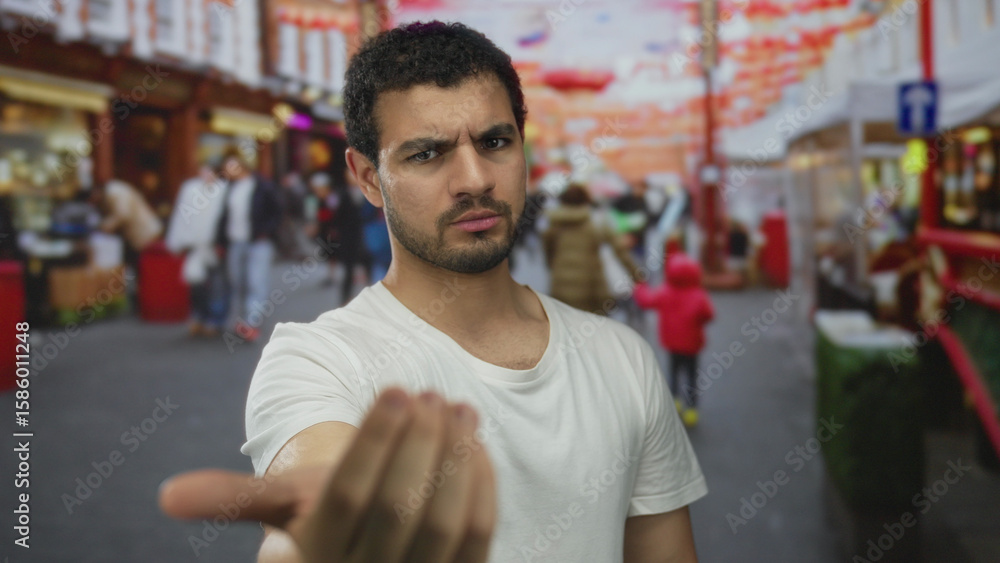 Obraz premium Man with serious expression beckons with outstretched hand and points finger on colorful street; invitation connection.