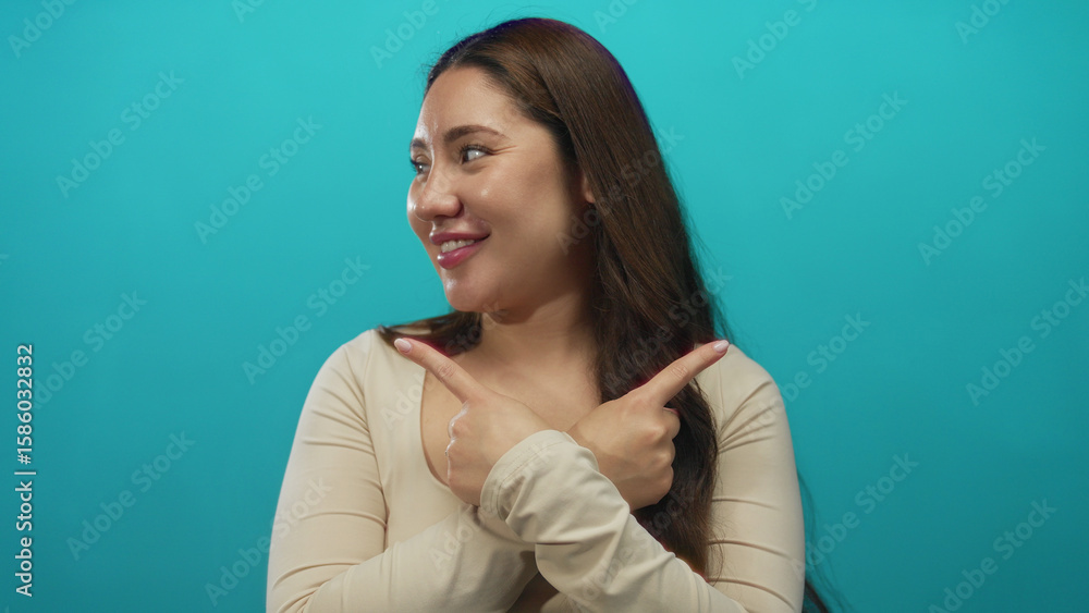 Fototapeta premium Hispanic woman pointing both index fingers crossed at chest in studio setting while smiling; rejection.