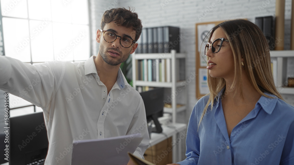 Obraz premium Man and woman discussing work in an office, showcasing teamwork in a modern workplace setting with documents and books in the background.