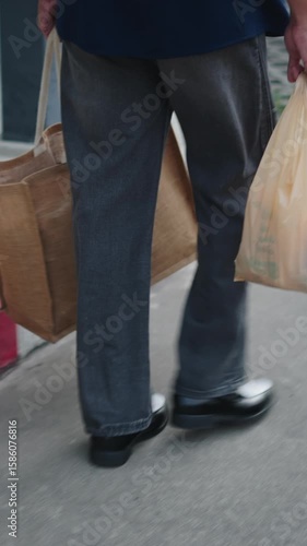 Urban pedestrians carrying a mix of reusable and plastic grocery bags as they walk on the sidewalk