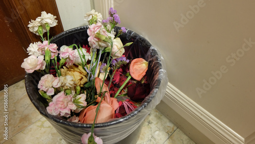 A bouquet of flowers in different varieties, thrown away into a rubbish bin. 
