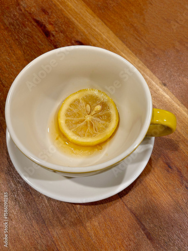 An empty tea cup with a slice of lemon and some leftover tea, on a wooden table.