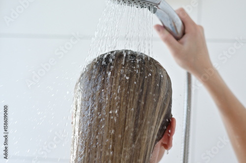 blond girl washes her hair with water in a shower on white background