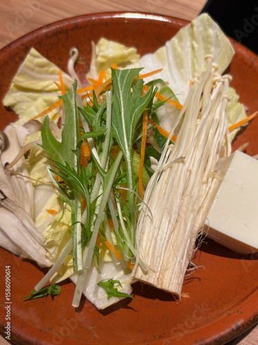 Closeup of a plate of raw vegetables and enoki mushroom, suitable to be used in Asian cuisine such as hotpot, shabu-shabu, nabe or sukiyaki.