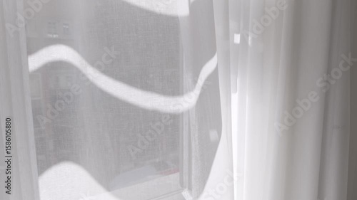 Close-up of white transparent curtain swaying by the wind on a sunny summer day. Modern home interior detail, fresh air coming through the open window. Light fabric moving slowly by the morning breeze