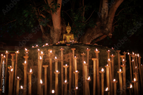 Foto golden buddha statue under bodhi tree surrounded by bamboo oil lamps glowing at