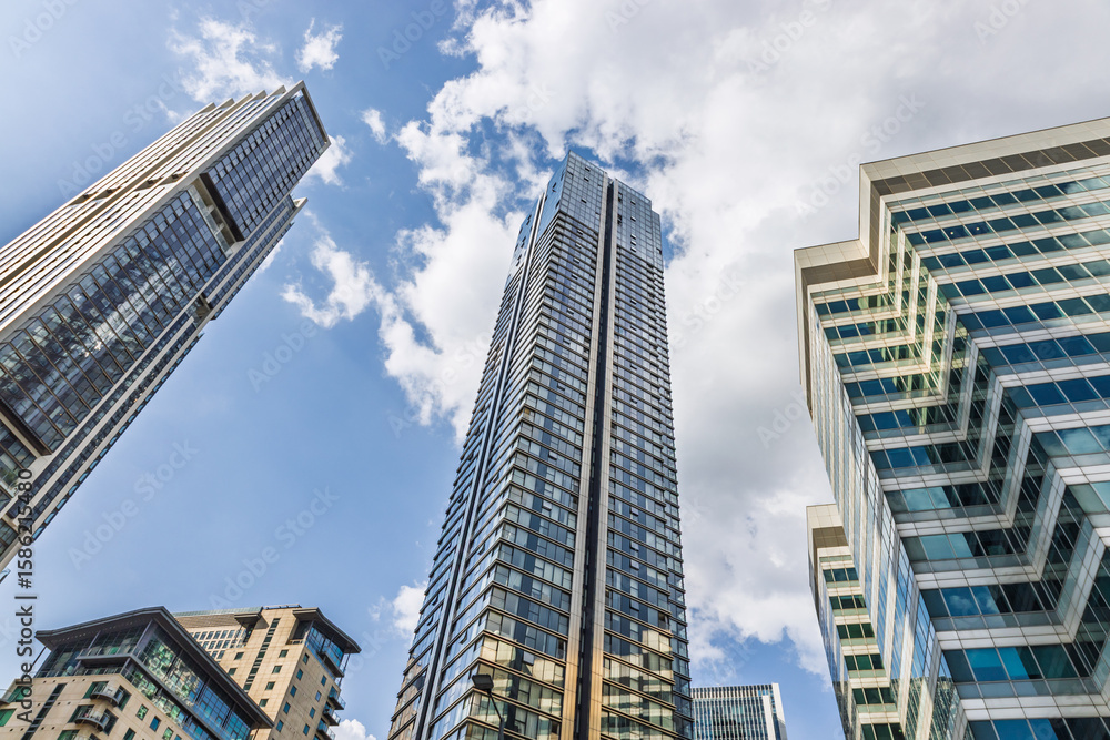 Obraz premium Low angle view of ultra modern glass skyscraper soaring into blue sky with reflective facade