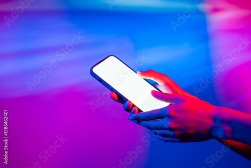 Hand interacting with smartphone under vibrant neon light