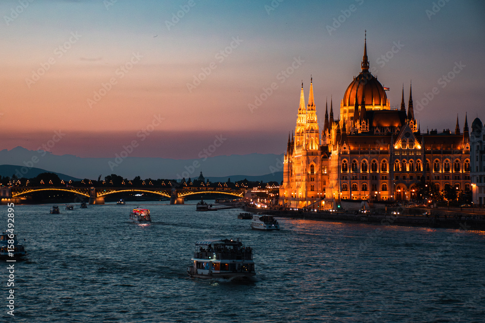 Obraz premium Illuminated Hungarian Parliament Building and boats on the Danube River at dusk in Budapest, Hungary