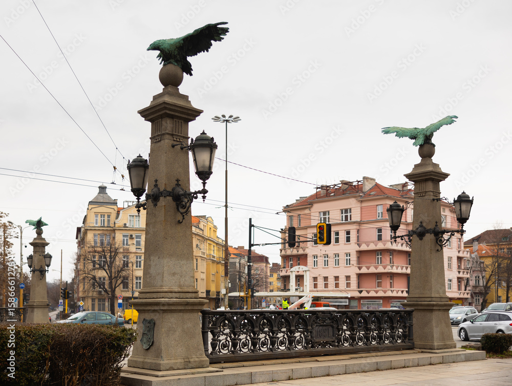 Fototapeta premium Busy traffic on ancient bridge over Perlovska River passes through Orlov Bridge. Historical architectural landmark. Bridges supports decorated with statues of eagles, symbol of freedom and defiance.