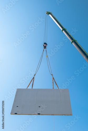 Prefabricated concrete wall being lifted by crane at construction site