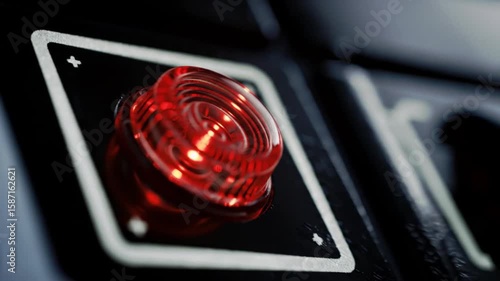 Close up of a red illuminated button on a black panel with a square frame around the button