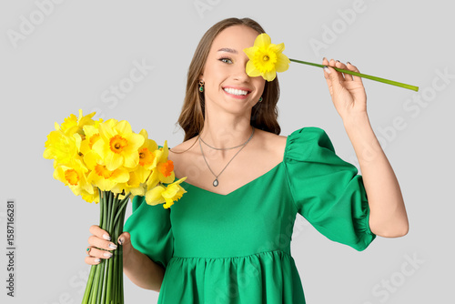Beautiful young woman with daffodils on light background