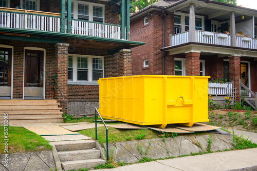 Photography A roll-off construction dumpster bright yellow outside a residential renovation project in an older neighourhood