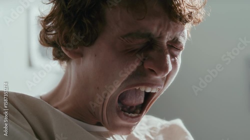 Frustrated male patient in straitjacket screaming during emotional breakdown in psychiatric hospital ward. Close-up view