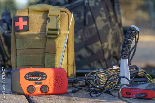 Survival kit including emergency crank radio, first aid kit, knife, paracord bracelet and power bank are lying on wooden table