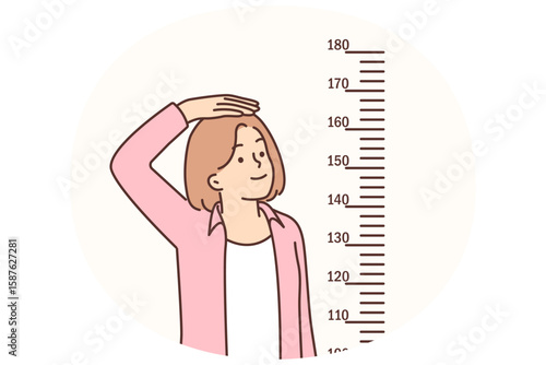 Teenage girl measures height standing near marks on wall, wanting to become tall