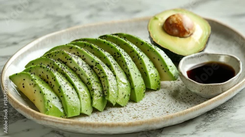 Avocado slice sprinkled with black sesame seed served on ceramic plate with half avocado and small bowl of sauce fresh green fruit healthy snack appetizer rich flavor smooth texture