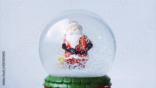 A festive New Year's scene featuring a snow-filled glass ornament with a miniature Santa Claus figurine inside. Gently shaken, the glittering snow swirls around, creating a magical and nostalgic
