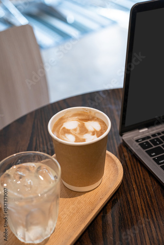 Close-up of Hot coffee latte with latte art milk foam in cup made of paper and laptop computer on wood desk office desk in coffee shop at the cafe,during business work concept