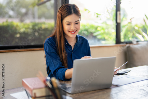 Free Download Young woman doing finance at home, holding paper document and looking at laptop. - GFXLoad