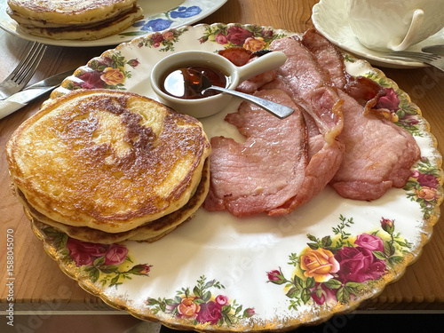 Delicious english breakfast plate featuring fluffy pancakes and crispy bacon served with maple syrup on a decorative floral plate, showcasing a delightful morning meal experience