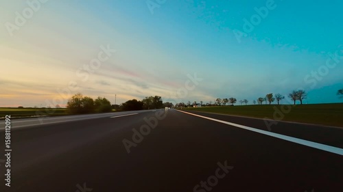 Driving Along Asphalt Road at Sunset With Golden Light and Trees Lining Way, breathtaking POV view. Car glides down quiet road at sunset, casting long shadows under warm glow of evening light