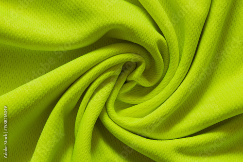 Bright lemon sports fabric twisted in the center as a background for design, close-up of folds, textile