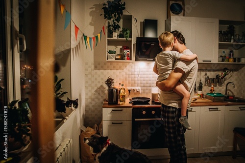 Foto dad holds son in his arms and cooks at the stove in the kitchen in the evening