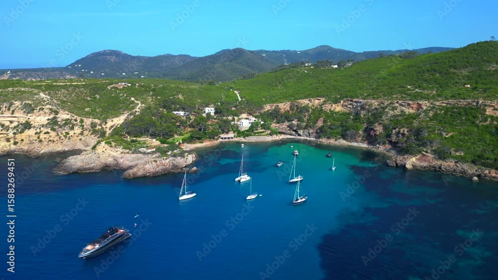 sailboats and yachts moored in turquoise waters of a bay on Ibiza, Spain, surrounded by lush greenery. Stunning aerial view flight overflight flyover drone sailboats and yachts moored in turquoise waters of a bay on Ibiza, Spain, surrounded by lush greenery. Stunning aerial view flight overflight flyover drone