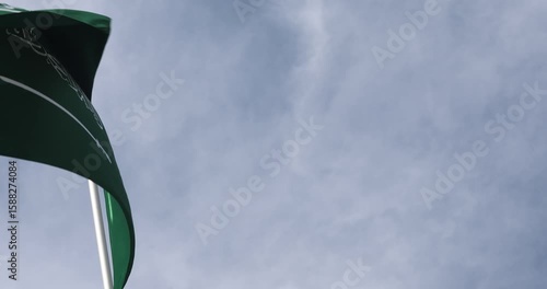 The Saudi Arabian flag is captured in close-up. The flag of Saudi Arabia, fluttering against the blue sky, is the national symbol of Saudi Arabia. Great for news.
