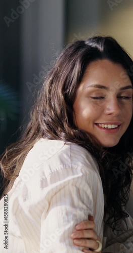 A young woman smiles at the camera. She's sitting at her desk in the office. An open laptop on the table in front of her