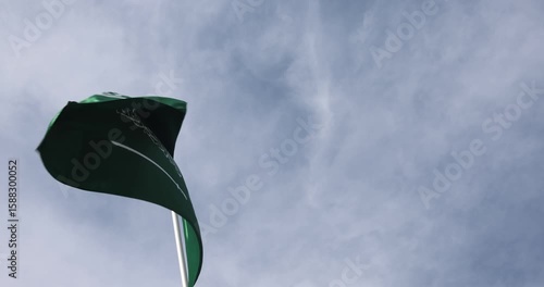The Saudi Arabian flag is captured in close-up. The flag of Saudi Arabia, fluttering against the blue sky, is the national symbol of Saudi Arabia. Great for news.