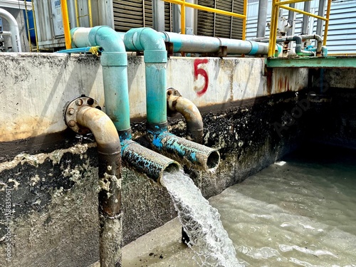 Industrial wastewater pipes discharging liquid into a treatment pond. Rusted pipes and algae buildup indicate long-term use. Water management in a factory setting.