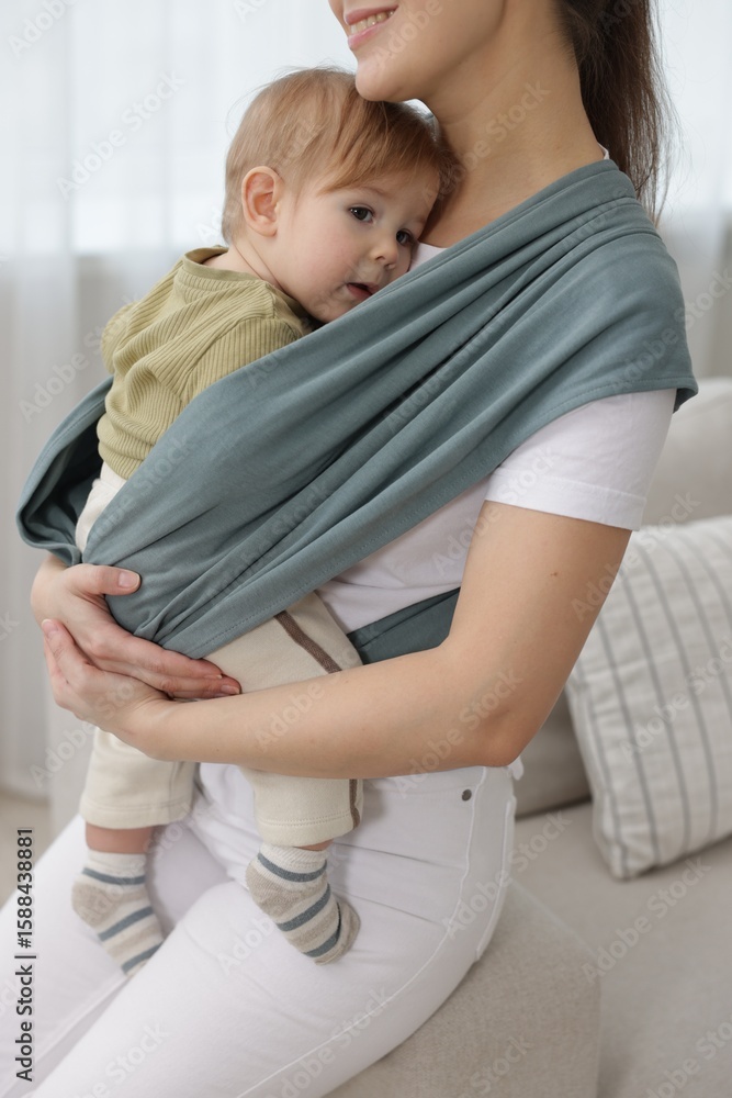 Fototapeta premium Mother holding her child in sling (baby carrier) at home, closeup
