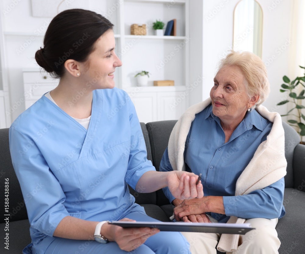 Fototapeta premium Nurse with clipboard examining senior woman indoors. Home health care service