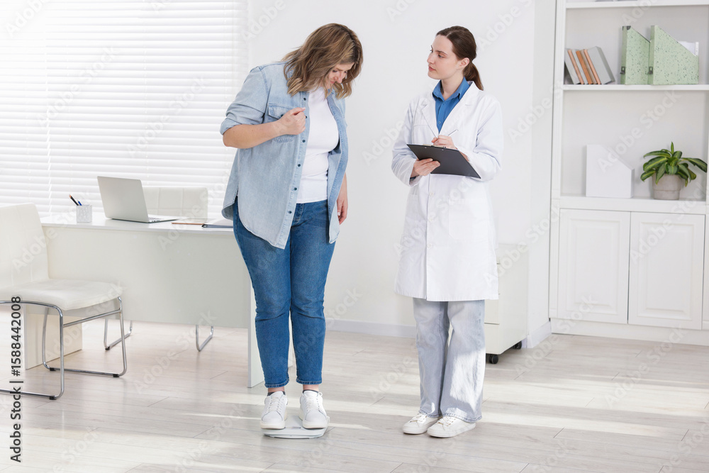 Weight loss. Overweight woman standing on scales during consultation with nutritionist in clinic Weight loss. Overweight woman standing on scales during consultation with nutritionist in clinic