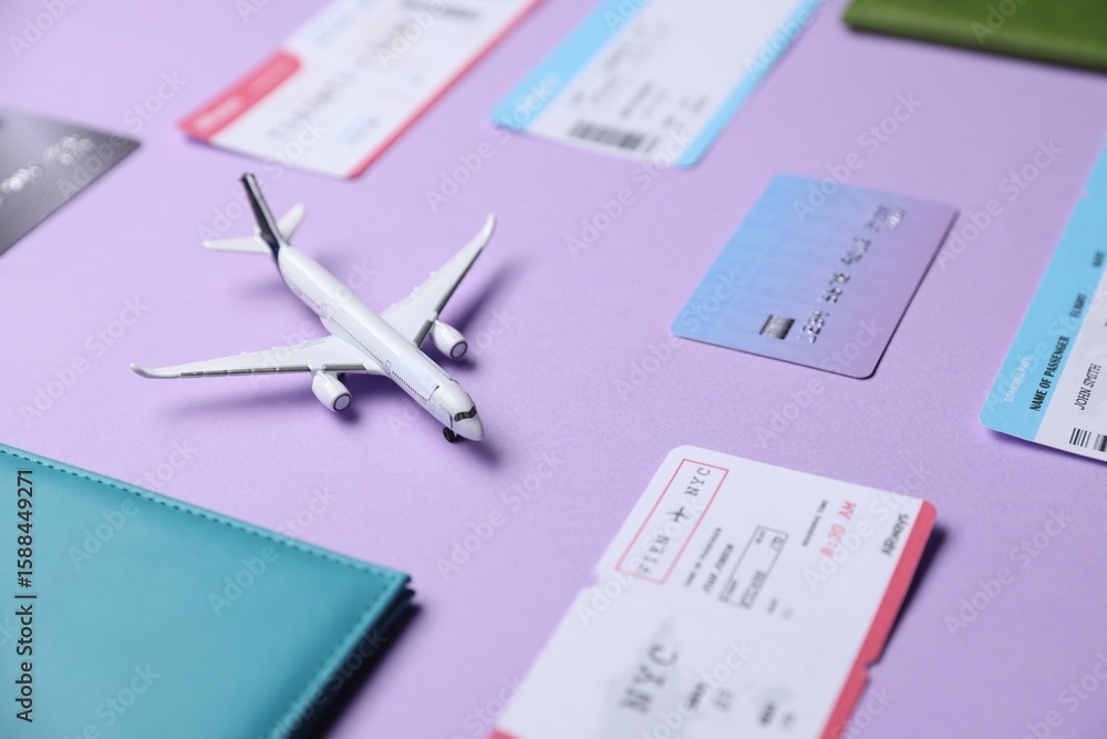 Fototapeta premium Airplane model, passport, credit card and flight tickets on violet background, closeup